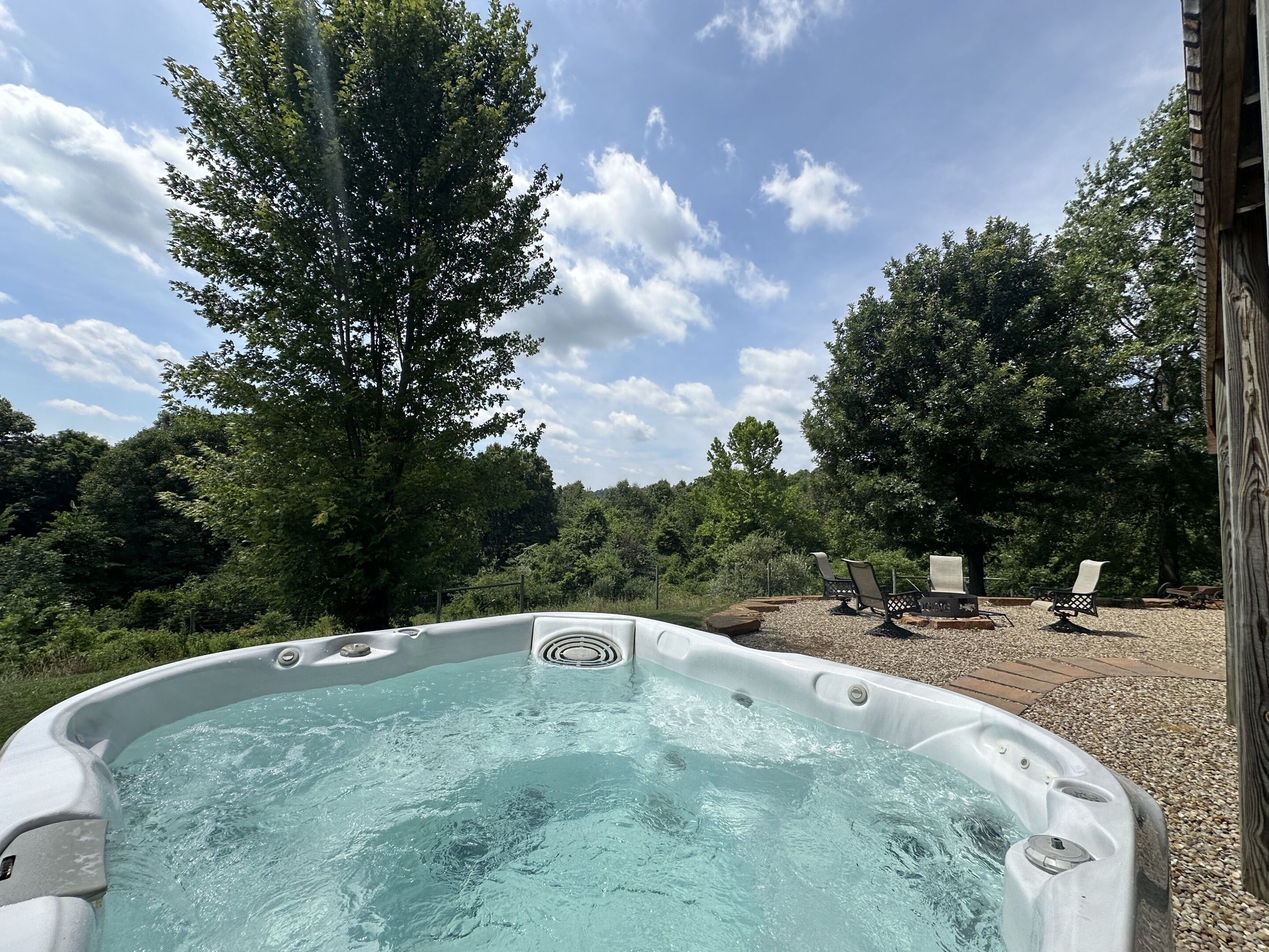 A hot tub with a view of a wooded area and a wooden deck with chairs.