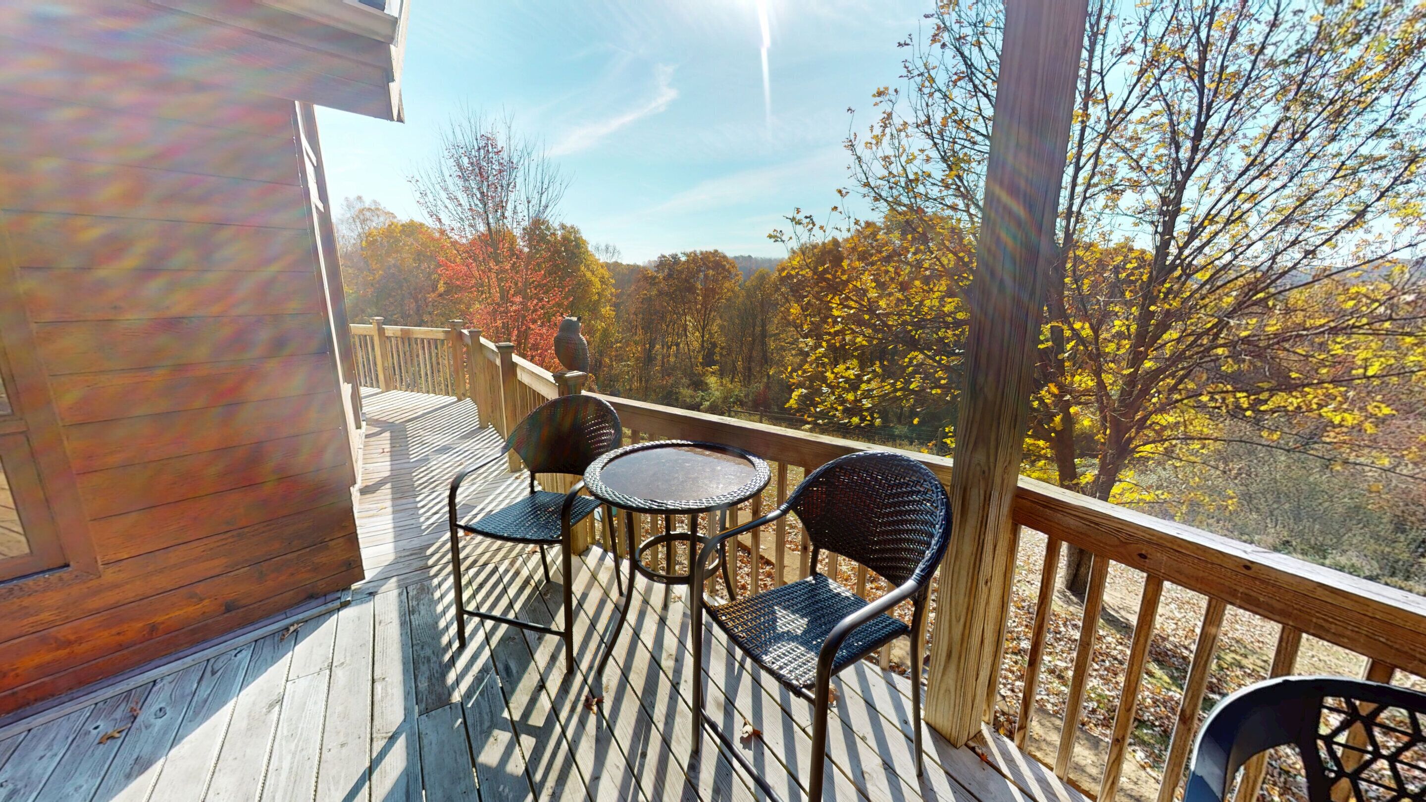 Eine Holzterrasse mit Tisch und Stühlen, mit Blick auf einen Wald im Herbstlaub.