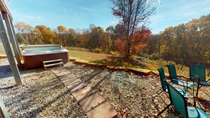 A hot tub with a wooden deck and steps leading to it, surrounded by gravel and autumn foliage.