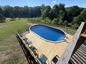 Una terraza de madera con una piscina rectangular, rodeada por una valla de madera y equipada con varias sillas de descanso.