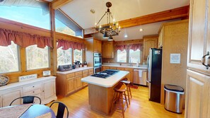 A spacious kitchen with wooden cabinets, a central island, and a dining area with a table and chairs. - Luxury Lodge on 125 acres on Hocking Hills Farm (Logan)