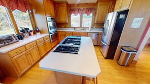 A kitchen with wooden cabinets, a stove, a refrigerator, and a window with a view of trees. - Luxury Lodge on 125 acres on Hocking Hills Farm (Logan)