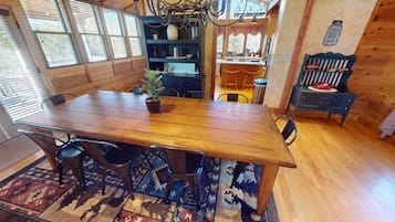 Une table à manger en bois, avec des chaises, une plante en pot et un coin cuisine équipé d’une cuisinière et d’un évier.
