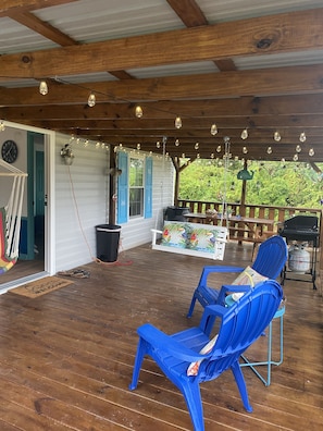 A covered porch with wooden beams, string lights, and blue chairs.