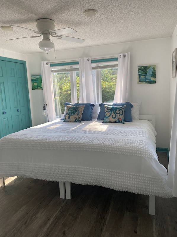Une chambre à coucher avec un grand lit, des rideaux blancs et un ventilateur de plafond.