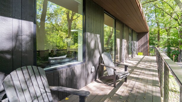 Eine überdachte Veranda mit zwei Adirondack-Stühlen, einer Bank und einem kleinen Tisch.