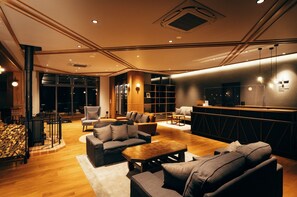 Relax in a comfortable lounge area with sofas, armchairs, and a bar counter, surrounded by a bookshelf and a fireplace.