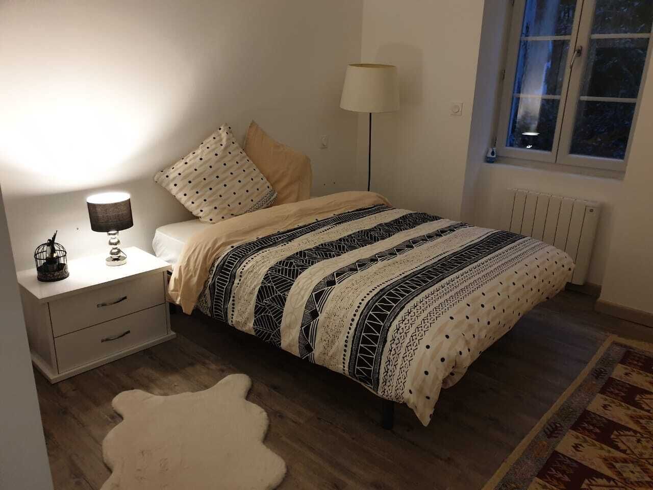 A bedroom with a bed, bedside table, lamp, and a window.