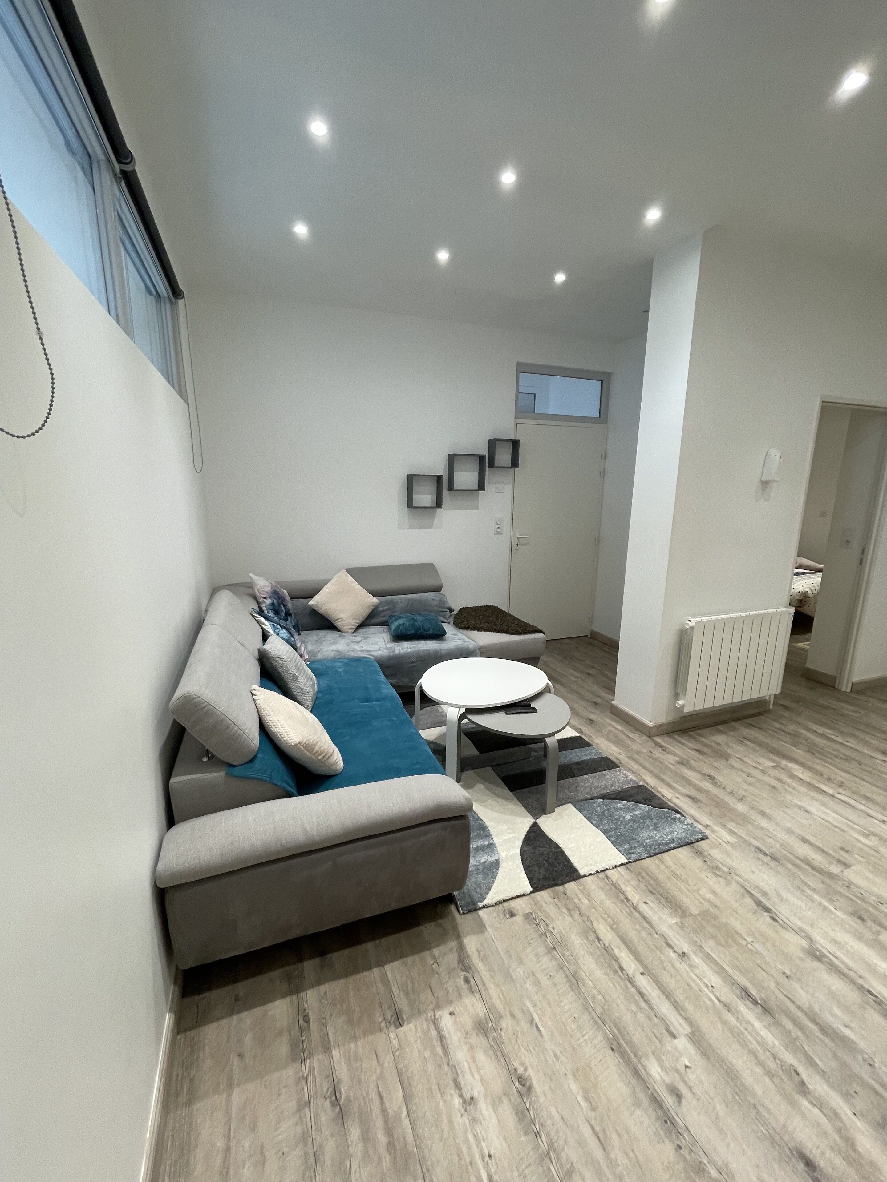 Una sala de estar moderna con un sofá gris, una manta azul y una pequeña mesa blanca.