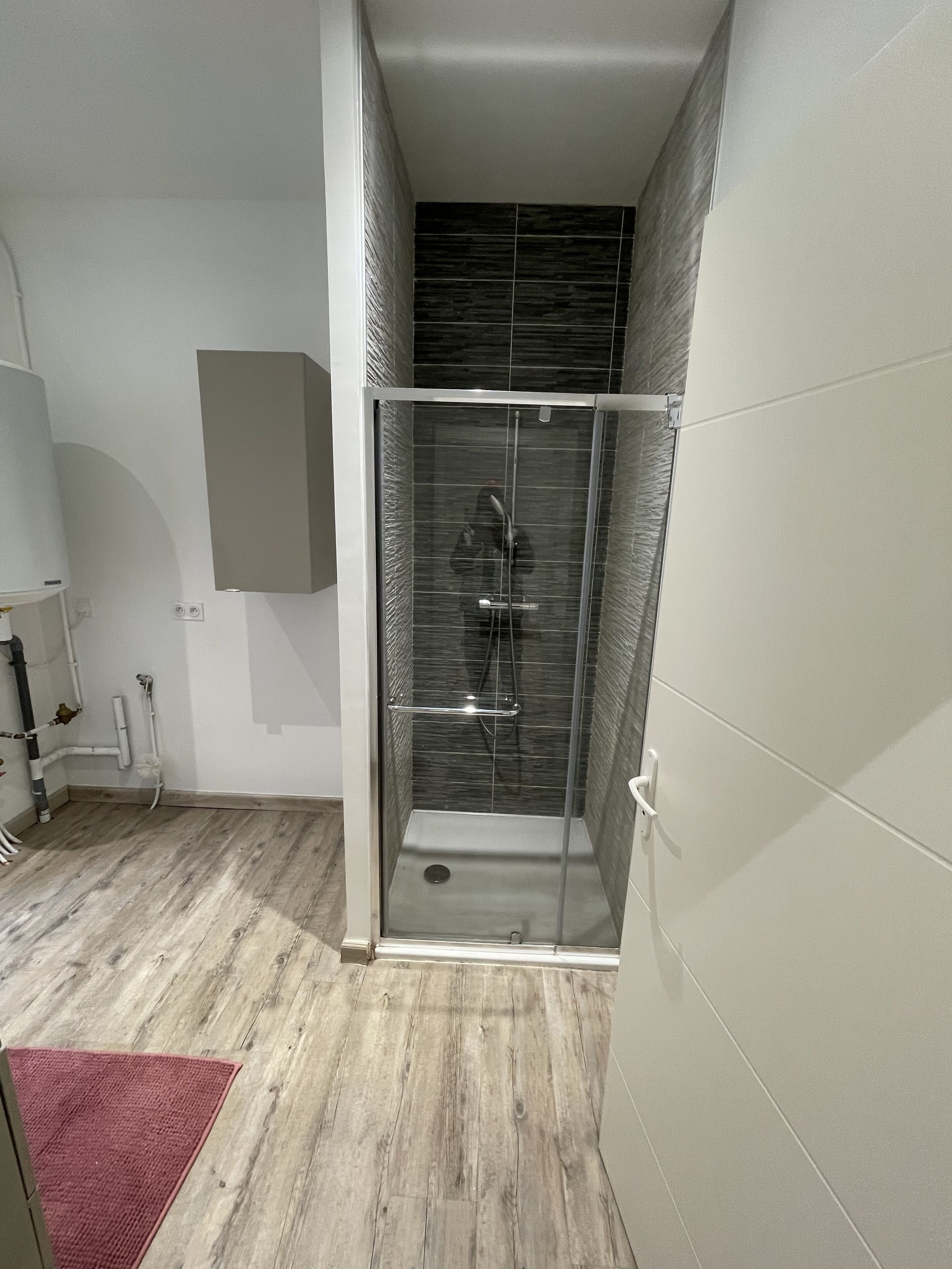 Een moderne badkamer met een douchecabine van glas, betegelde wanden en een houten vloer.