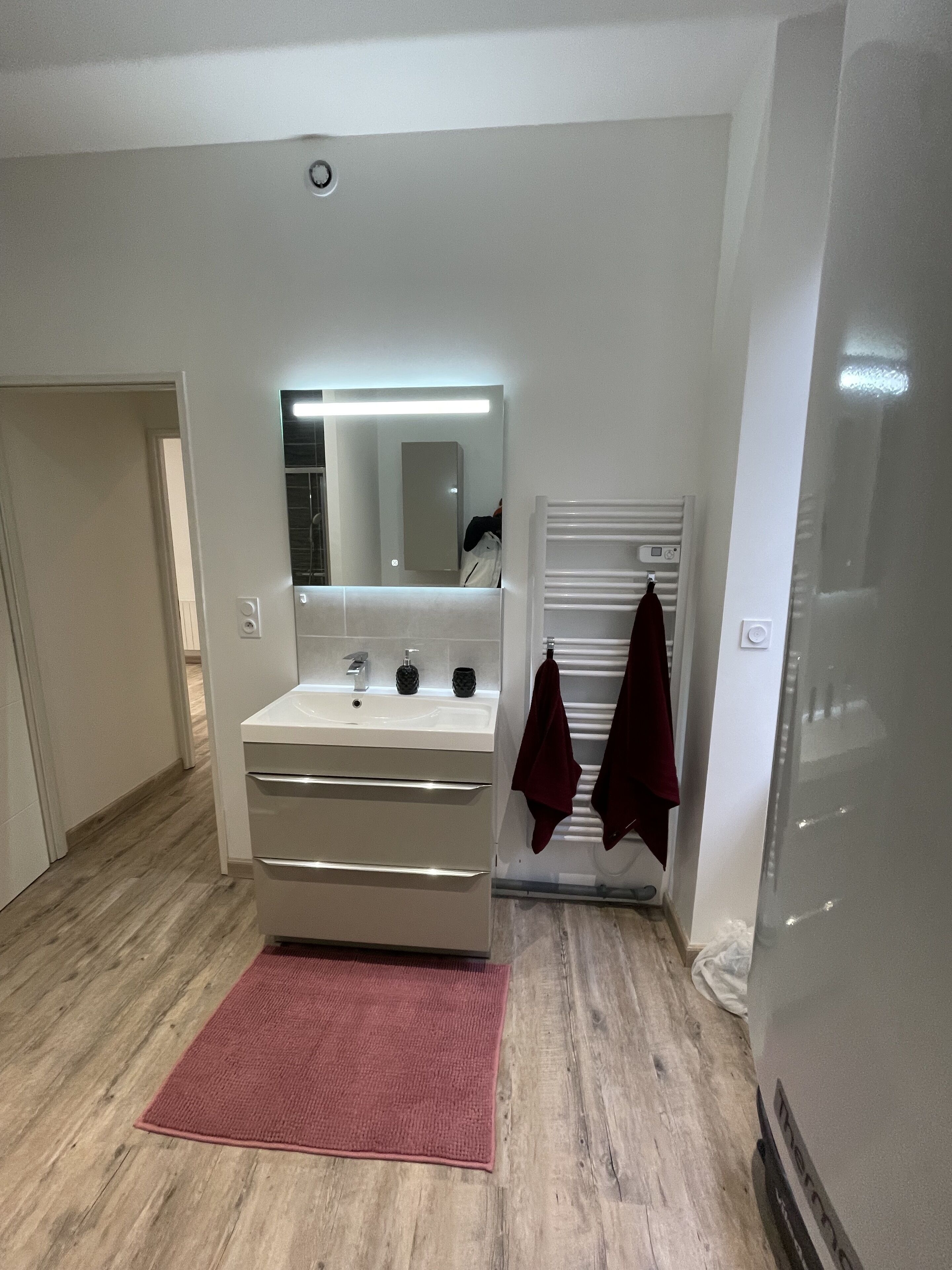 Un baño moderno con tocador blanco, espejo y toalla roja.