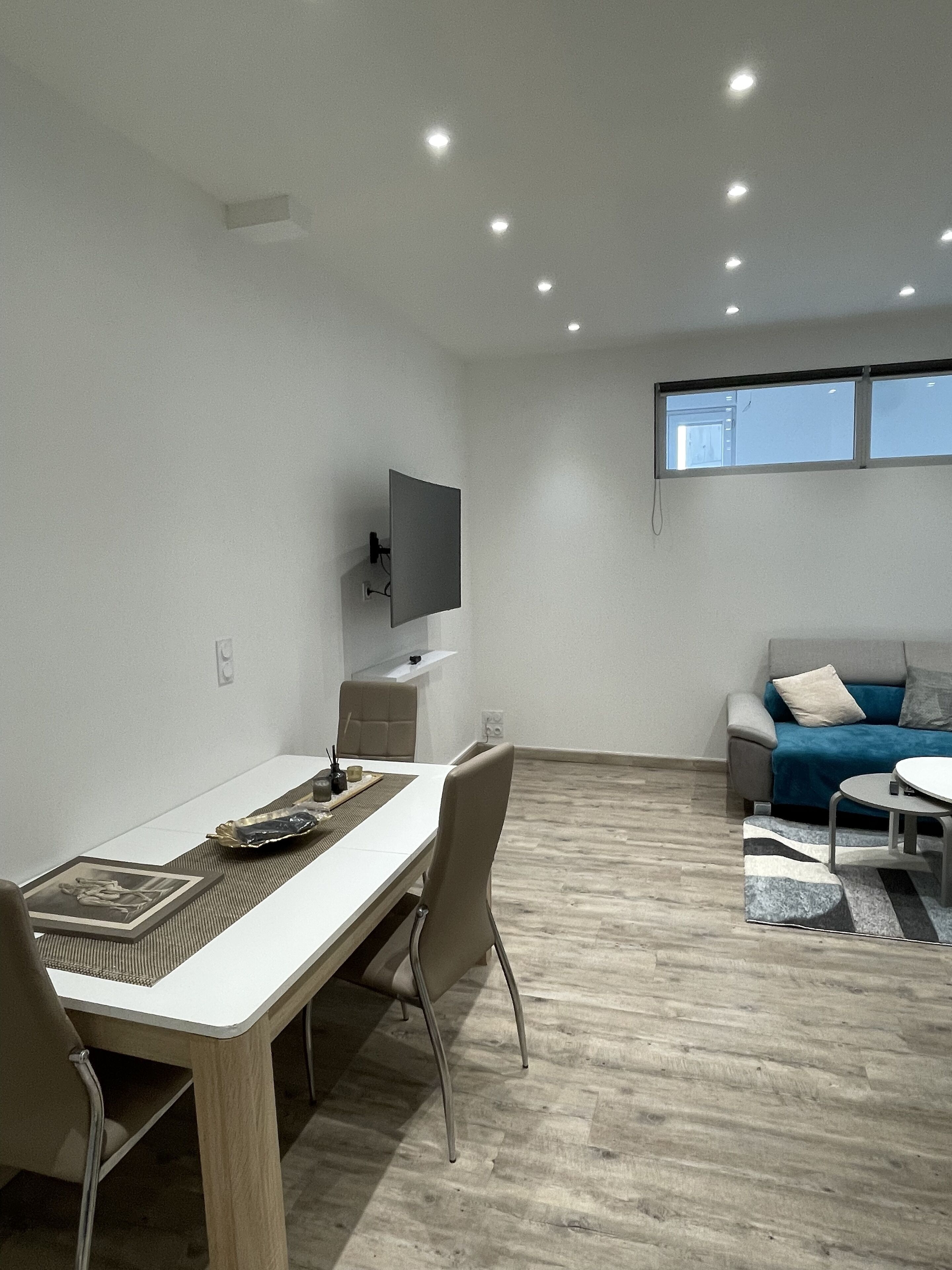 Una sala de estar moderna con comedor, un televisor de pantalla plana montado en la pared y un ventanal que proporciona luz natural.