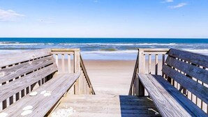 Ein Holzsteg führt zu einem Strand mit freiem Blick auf das Meer.