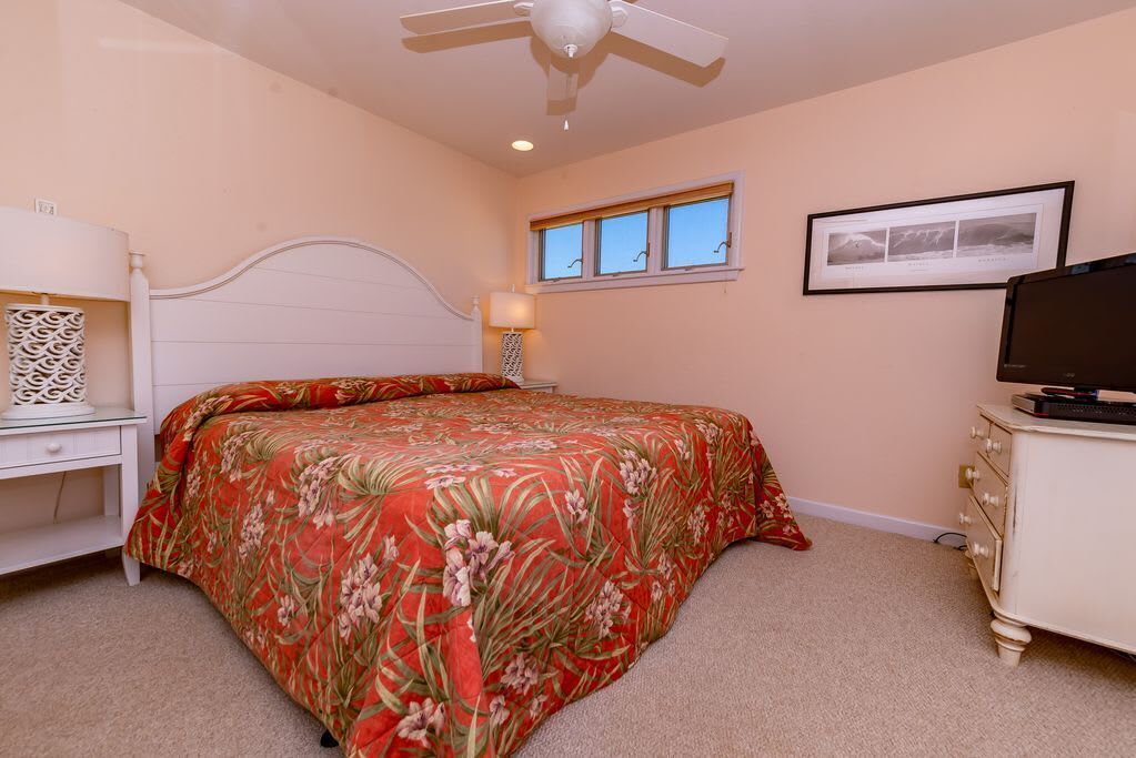A bedroom with a bed, a nightstand, a dresser, a ceiling fan, a window, and a framed picture on the wall.