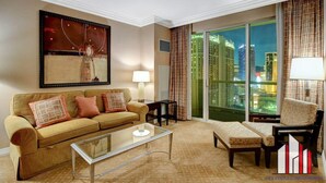 Uma sala de estar moderna com sofá, poltrona e um banquinho, uma mesa de centro de vidro e um quadro grande na parede.