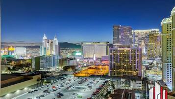 A cityscape at night with illuminated buildings, a parking lot, and a view of the mountains in the background.