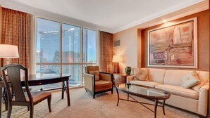 A hotel room with a dining table, two chairs, a sofa, a coffee table, and a large window with a city view. - MGM Signature- Studio Workdesk Strip View Jacuzzi (Las Vegas)