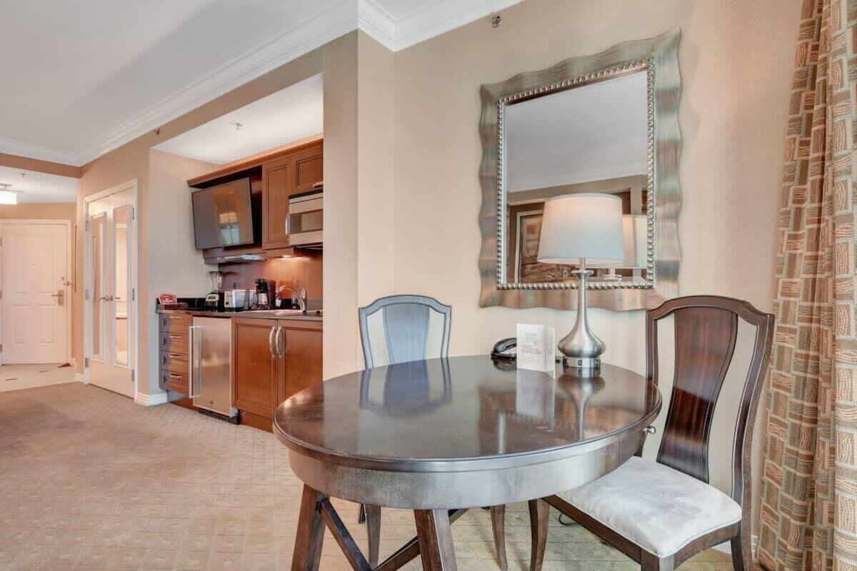 A dining area with a round table, two chairs, a mirror, and a lamp.