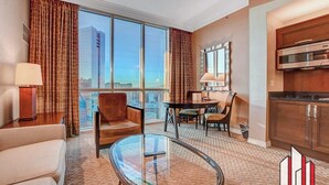 A hotel room with a large window, a dining area, a kitchen, and a seating area with a glass table. - MGM Signature-30-719 Strip View Jacuzzi Studio (Las Vegas)