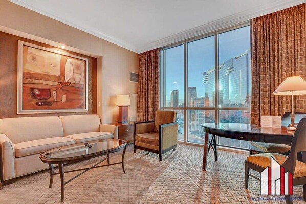 A hotel room with a large window, a sofa, a chair, a coffee table, and a painting on the wall. - MGM Signature-30-719 Strip View Jacuzzi Studio (Las Vegas)