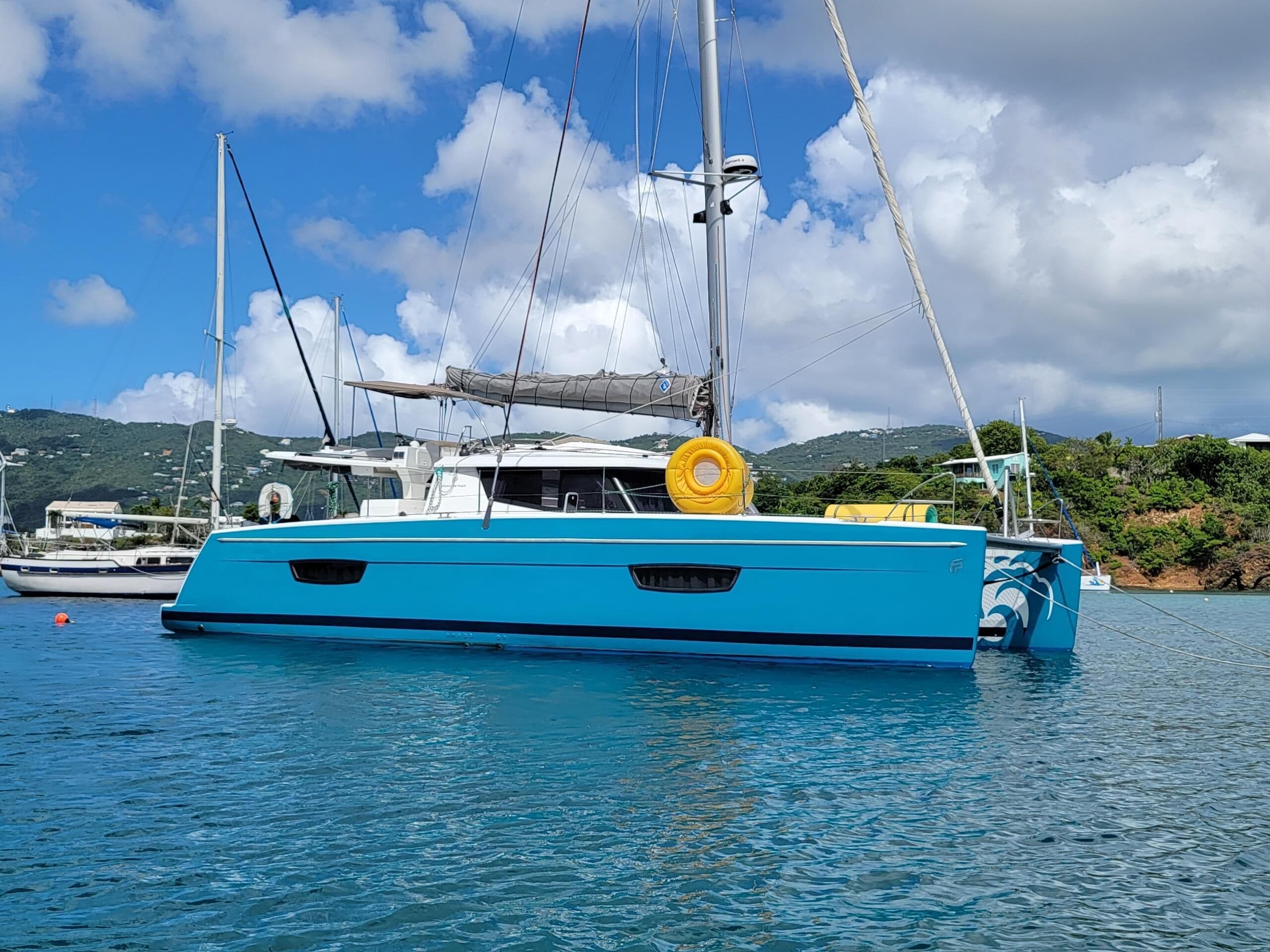 A large blue yacht docked at a marina with a clear sky and hills in the background.