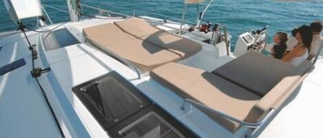 A sailboat with a sun deck featuring lounge chairs and a small enclosed area with a window.