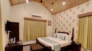 A bedroom with a wooden bed, a bedside table, a bench, a TV, and an air conditioner. - Keshav Resort (Udaipur)
