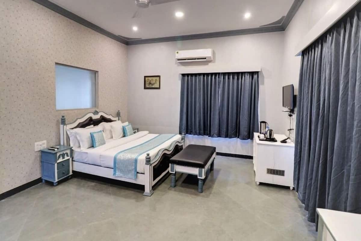 A modern hotel room with a bed, bedside table, a desk with a chair, an air conditioning unit, and a window with curtains.