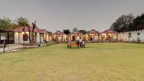 A row of stone cottages with red-tiled roofs and a grassy courtyard. - Keshav Resort (Udaipur)