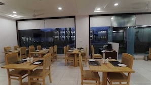 A dining area with wooden tables and chairs, large windows with blinds, and a ceiling fan. - Keshav Resort (Udaipur)