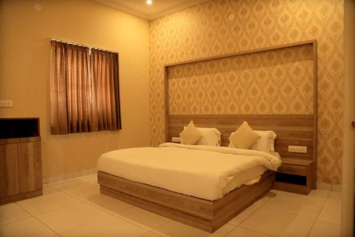 A bedroom with a wooden bed frame, a headboard with a patterned wallpaper, a bedside table, and a curtain on the window.