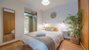 A bedroom with a bed, bedside tables, a mirror, a wall clock, and a potted plant.