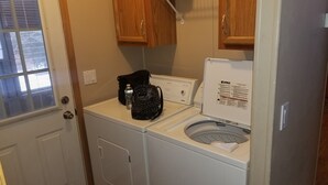 A compact laundry area with a front-loading washing machine and dryer, wooden cabinets above, and a window with blinds.