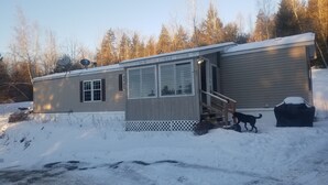 A single-story cabin with a covered porch, a small deck, and a snow-covered yard.