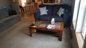 A living room with a grey sofa, a wooden coffee table, and a carpeted floor.