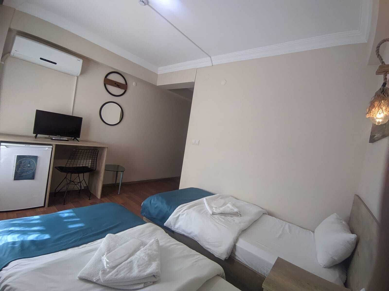 A hotel room with two beds, a desk with a computer, a small refrigerator, and a TV.