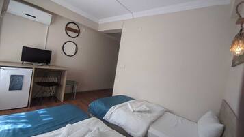 A hotel room with two beds, a desk with a computer, a small refrigerator, and a TV.