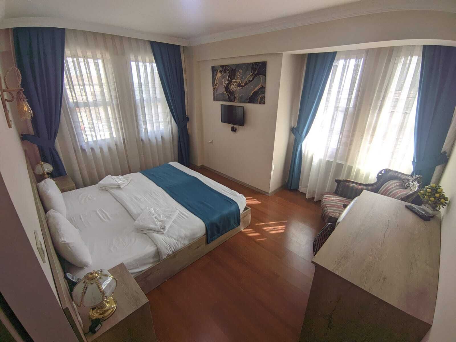 Habitación de hotel con cama, escritorio, silla, televisor en la pared y ventana con cortinas.