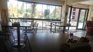En restaurant med flere borde og stole, store vinduer med udsigt udad, og en lyserød stol i hjørnet.