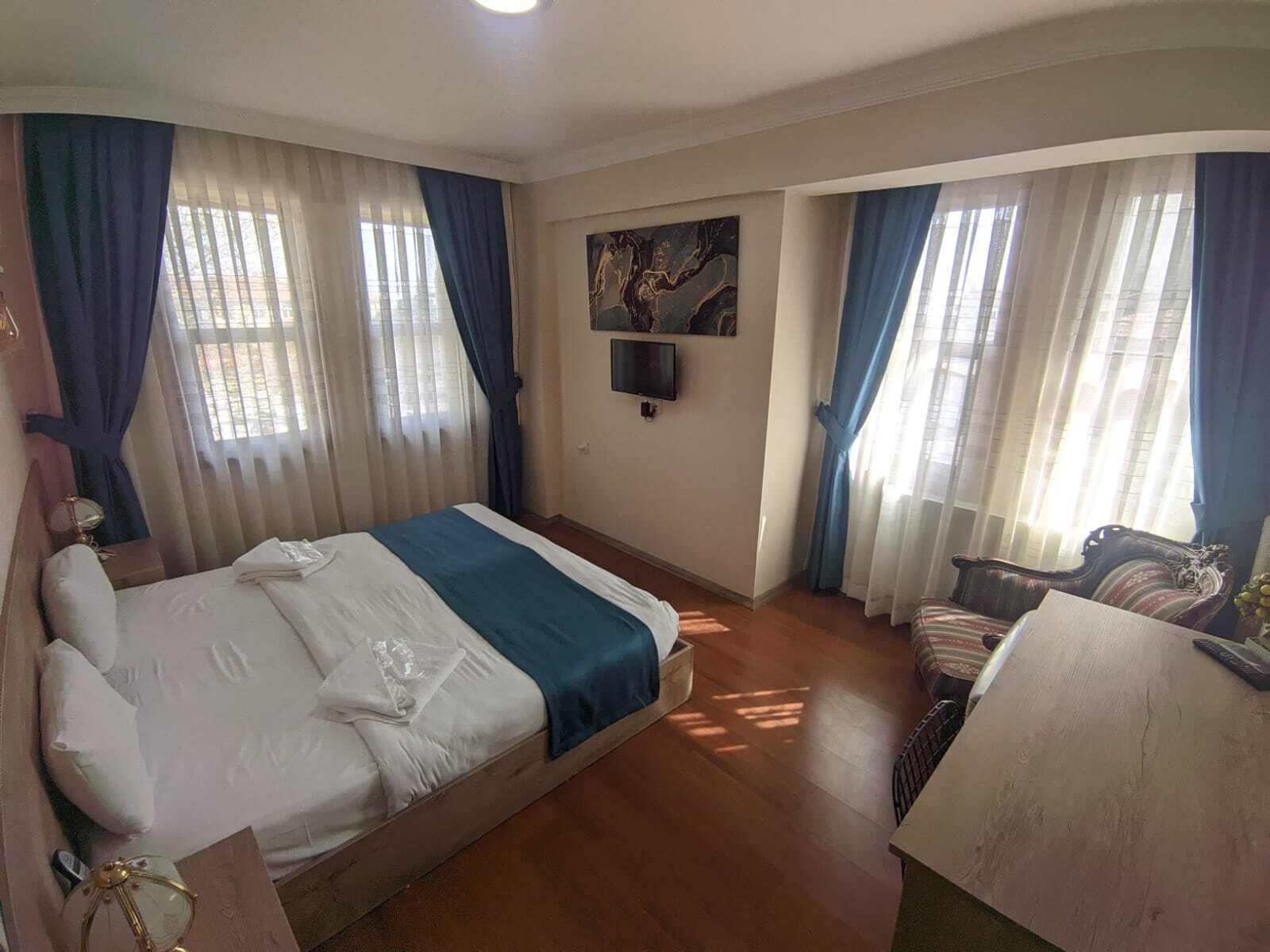Une chambre d’hôtel avec un lit, un bureau et une chaise. Il y a un tableau au mur et une fenêtre avec des rideaux.