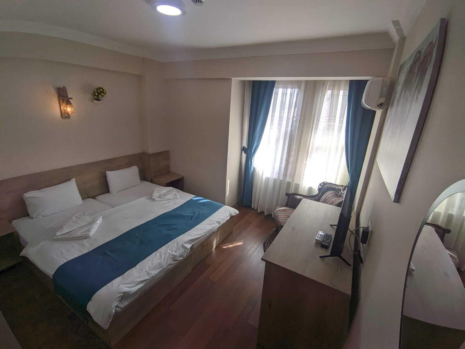 Et hotelværelse med en seng, et skrivebord og et vindue med gardiner.