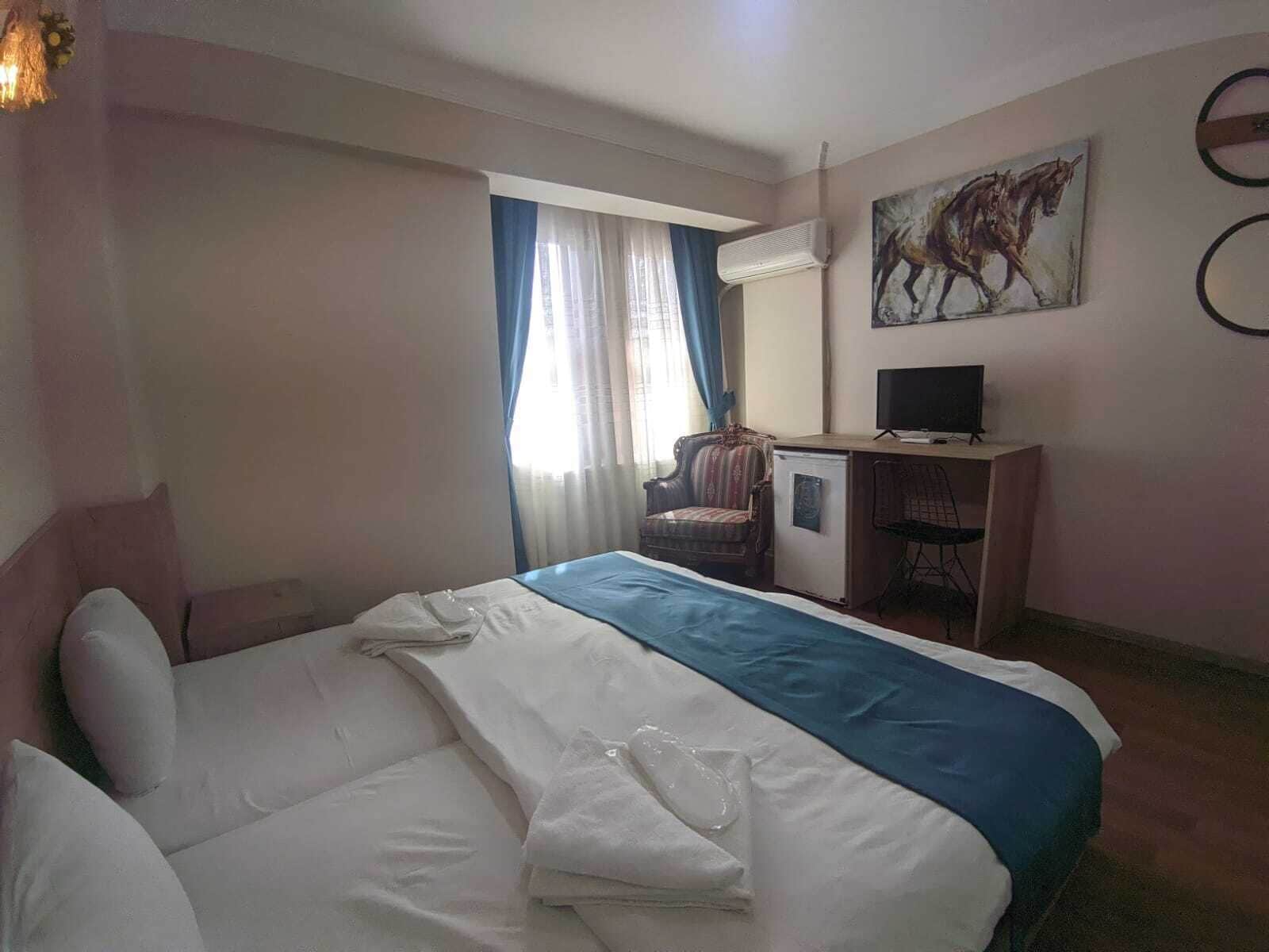 A hotel room with a bed, a desk, a chair, a television, and a painting on the wall.