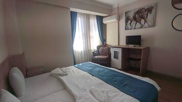 A hotel room with a bed, a desk, a chair, a television, and a painting on the wall.