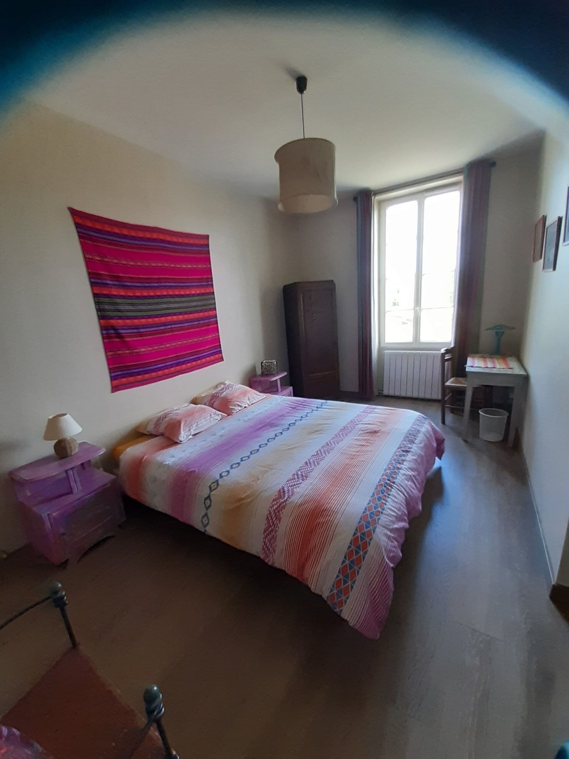 Ein Schlafzimmer mit Bett, Schminktisch, Nachttisch, Fenster und Heizkörper.