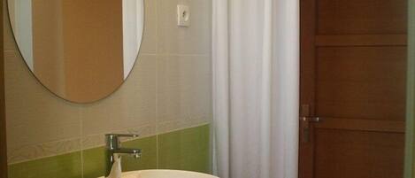 Un baño con un espejo redondo, un lavabo blanco y un mueble de tocador de madera.