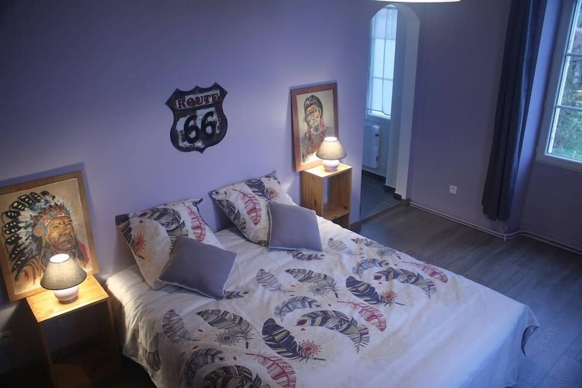 Une chambre à coucher avec un lit, deux tables de chevet, une horloge murale et une fenêtre.