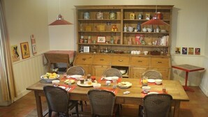 Un comedor con una mesa de madera dispuesta para cuatro personas, rodeada de sillas de mimbre. En el fondo, un armario de madera con distintos utensilios de cocina.