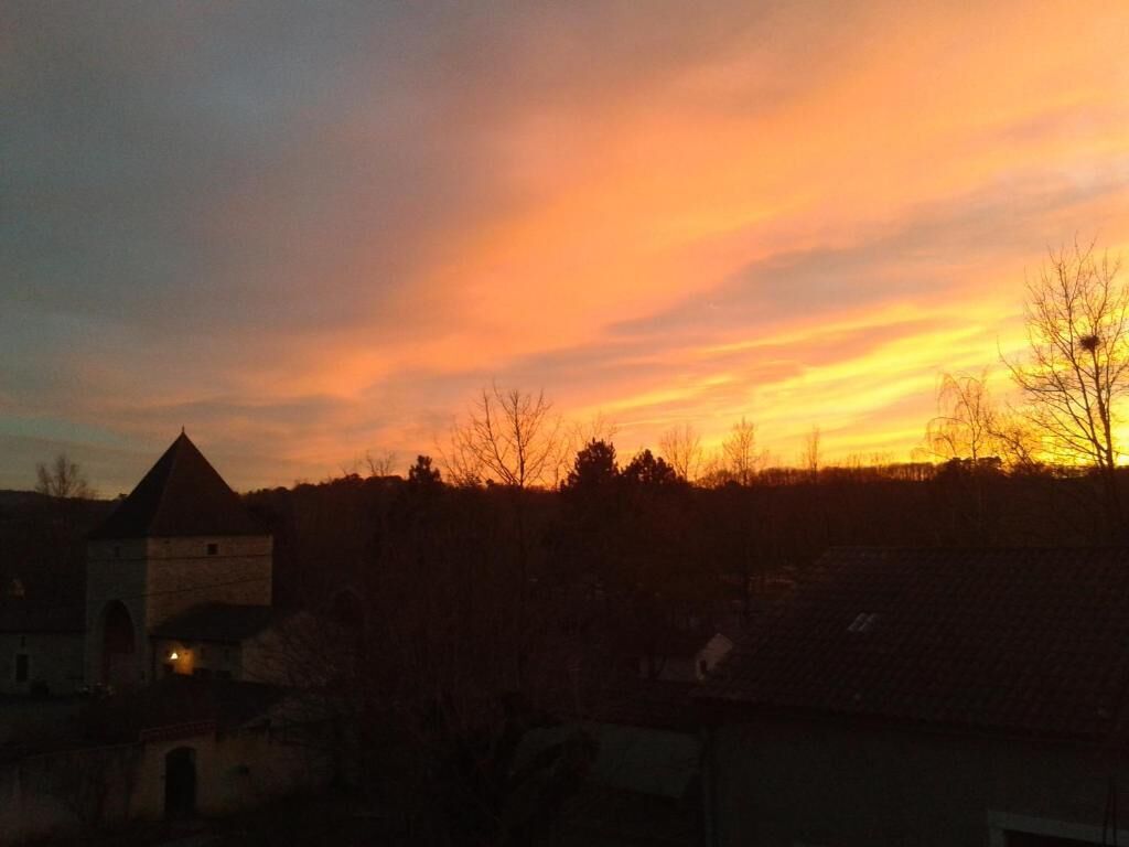 A rural landscape at sunset with a building and trees silhouetted against a colorful sky.