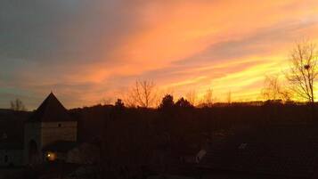 A rural landscape at sunset with a building and trees silhouetted against a colorful sky.