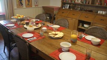 Une table à manger dressée avec des assiettes, des bols et des verres, entourée de chaises en osier.